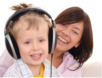 Photo of a little boy, wearing headphones, and a woman.